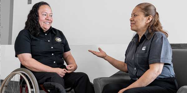A Cummins employee using a wheelchair talks with another employee seated in an office.