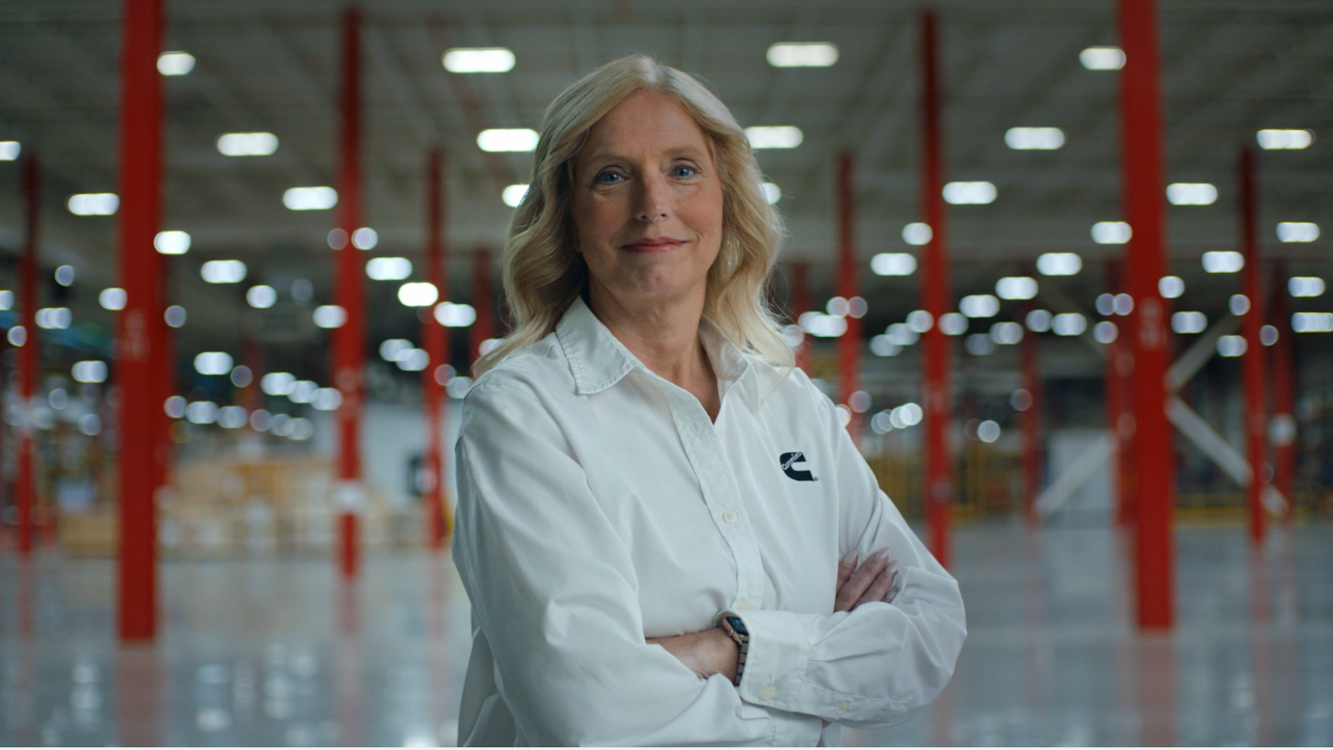 A Cummins employee stands confidently in a facility wearing a white dress shirt with Cummins logo.