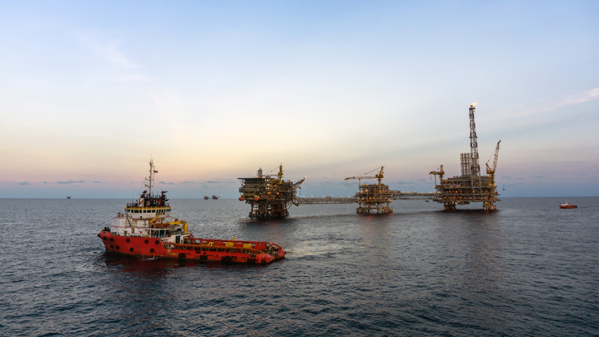 A supply vessel approaches an offshore oil platform at sunset