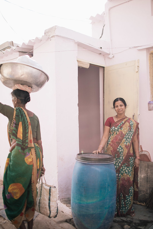 Woman standing near home with tall blue can for holding water