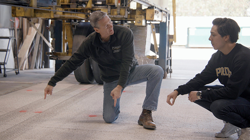 A professor and student examining a slab of concrete pavement 