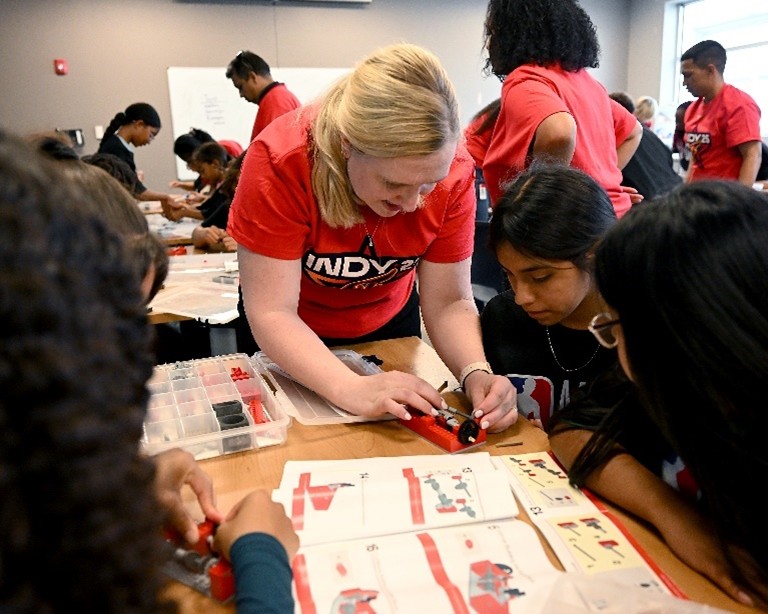 A Cummins volunteer works with students to build a 2-cylinder Lego diesel engine model