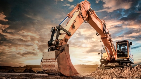 excavator shown digging up dirt at sunset