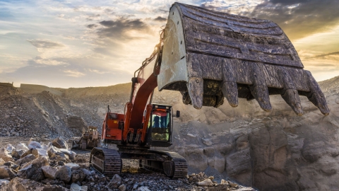 large mining excavator digging up rocks and gravel at sunset