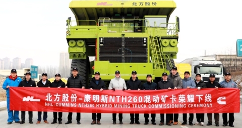 Group of Cummins employees shown holding a red banner in front of a mining hybrid truck