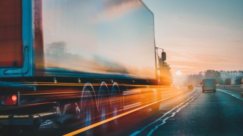 semi truck driving on a highway towards a sunset