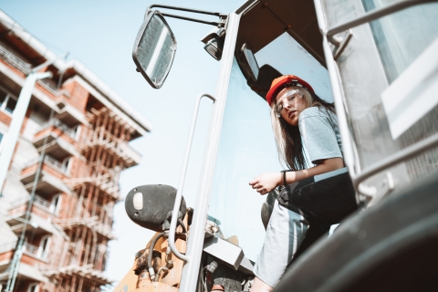 A construction worker sits in the cab of a vehicle in front of an appartment building.