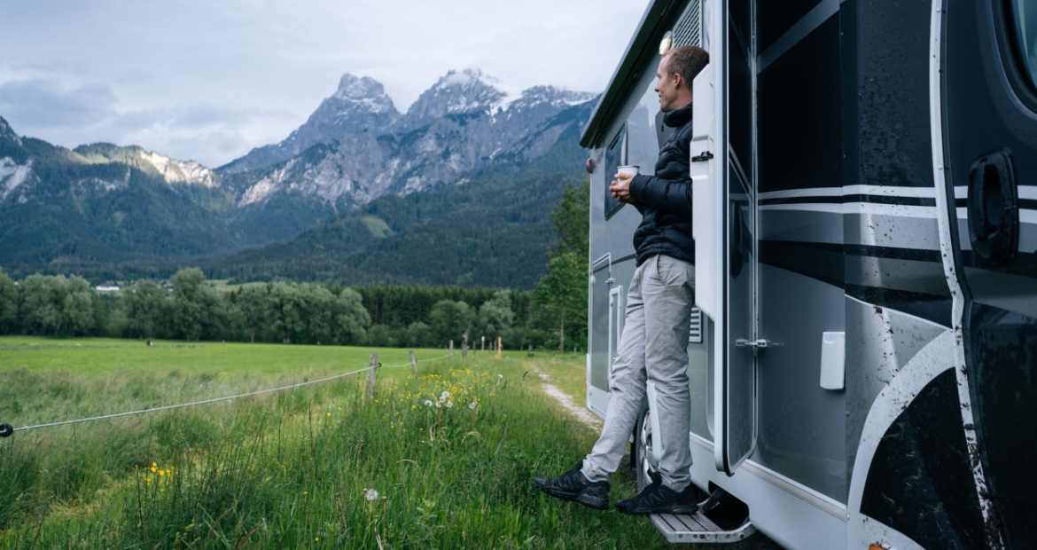 A man stands in his rv doorway and looks out onto open mountain range
