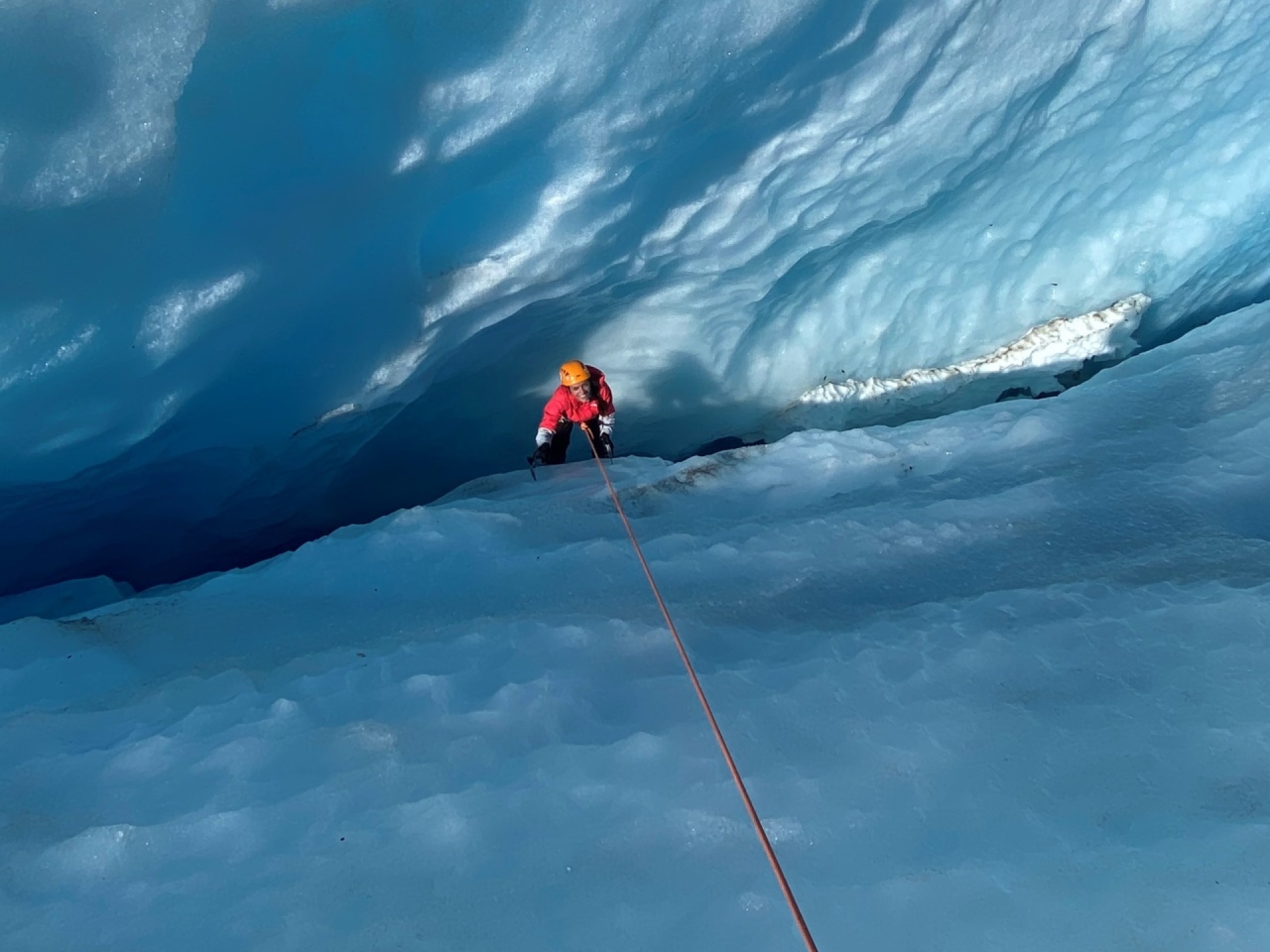 person climbing wall of glacier ice