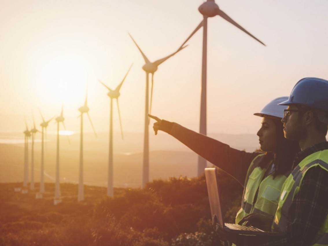 Workers collaborate in a windfarm at dawn.