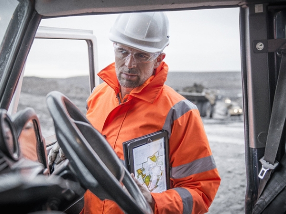 miner with hardhat and protective equipment examines tablet in truck