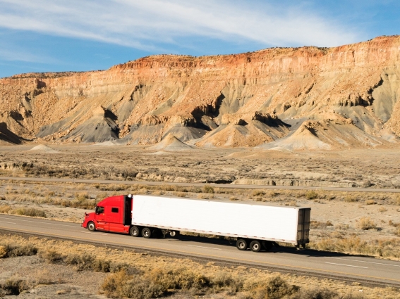 Truck driving alone in desert with mountain in the background