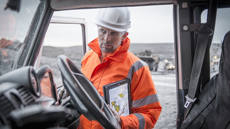 miner with hardhat and protective equipment examines tablet in truck