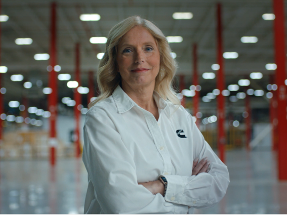 A Cummins employee stands confidently in a facility wearing a white dress shirt with Cummins logo.